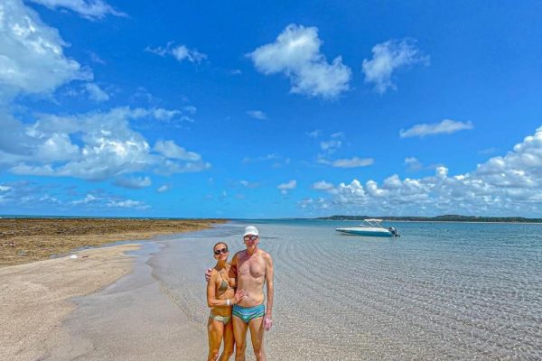 Casal no banco de areia em Japaratinga, de fundo a imagem da lancha